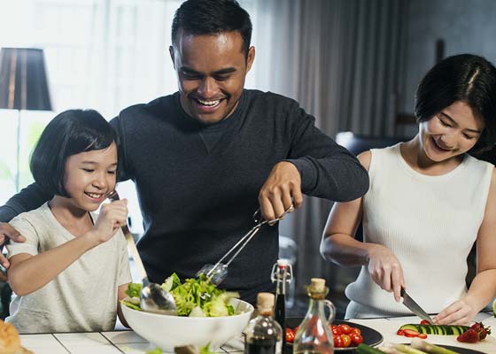 Un couple et leur fille préparent une salade à la maison.