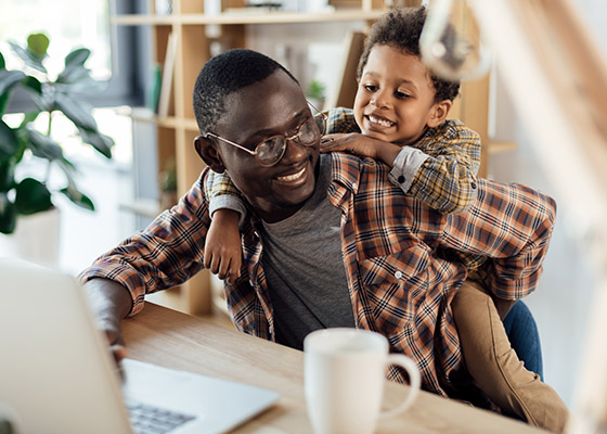 Father working at a desk in his home with his son sitting on his back.