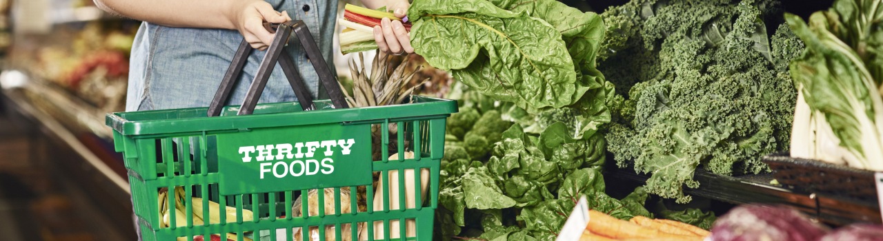 In this image, a lady holds a Thrifty food basket and vegetables in her hands.