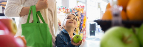 This banner image shows a child holding a green apple in his hand, watching his mother, and smiling.